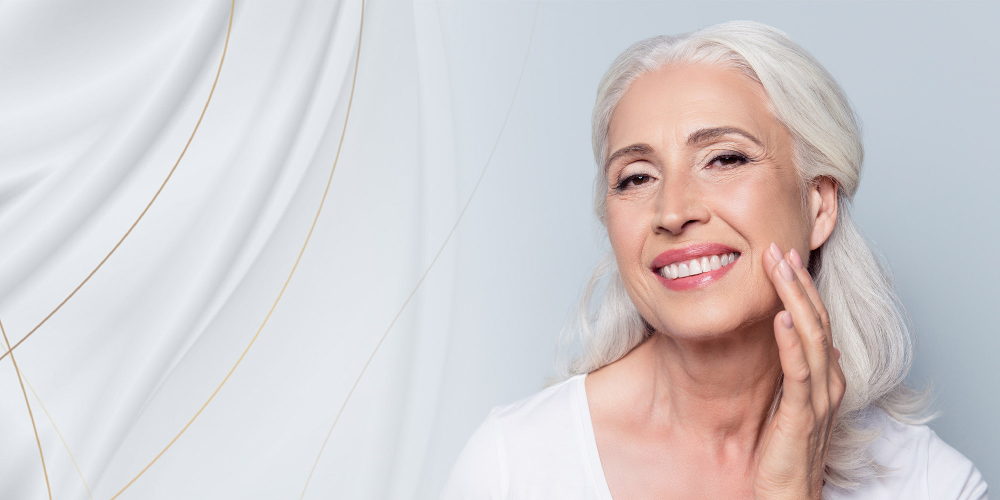 Lady with white hair smiling looking forward touching her face