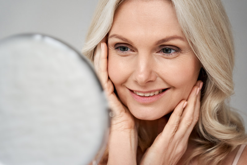 Lady with blonde hair smiling looking into a mirror happy